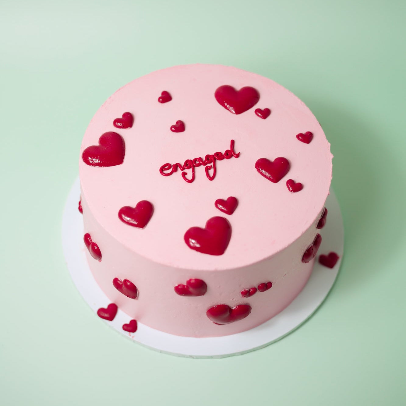 A pink round cake with red heart decorations and custom text