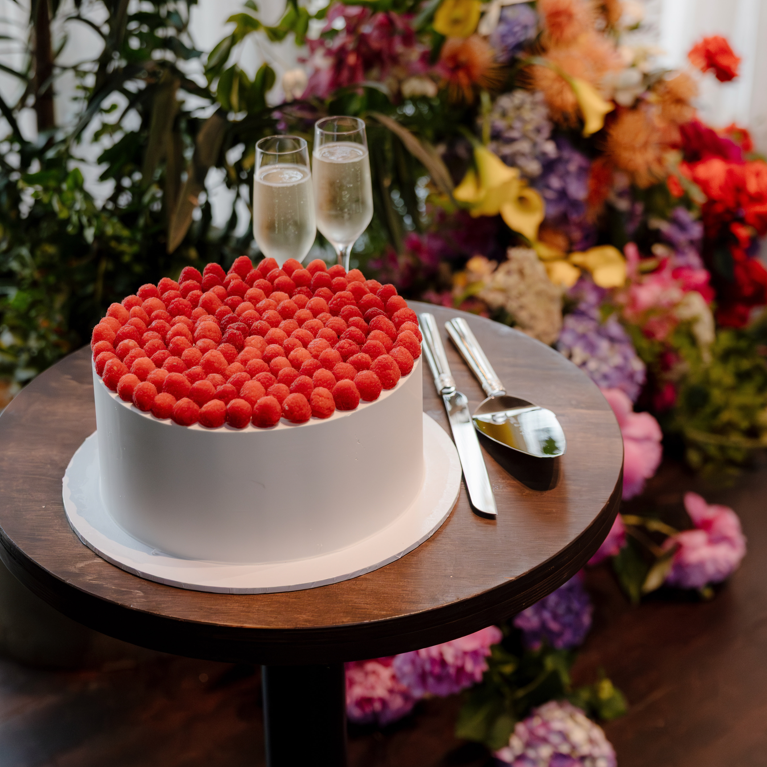 White cake with fresh red berry topping on a wooden table with floral decorations for a melbourne wedding.