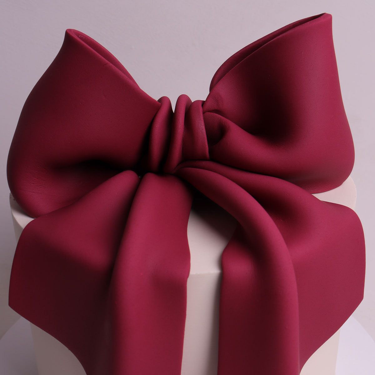 oversized burgundy fondant bow sitting on buttercream cake for birthday and baby shower events in Mellbourne.