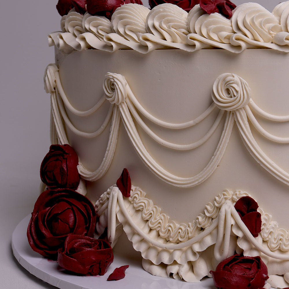 Vintage-style buttercream wedding cake with draped piping, ruffles and red rose details