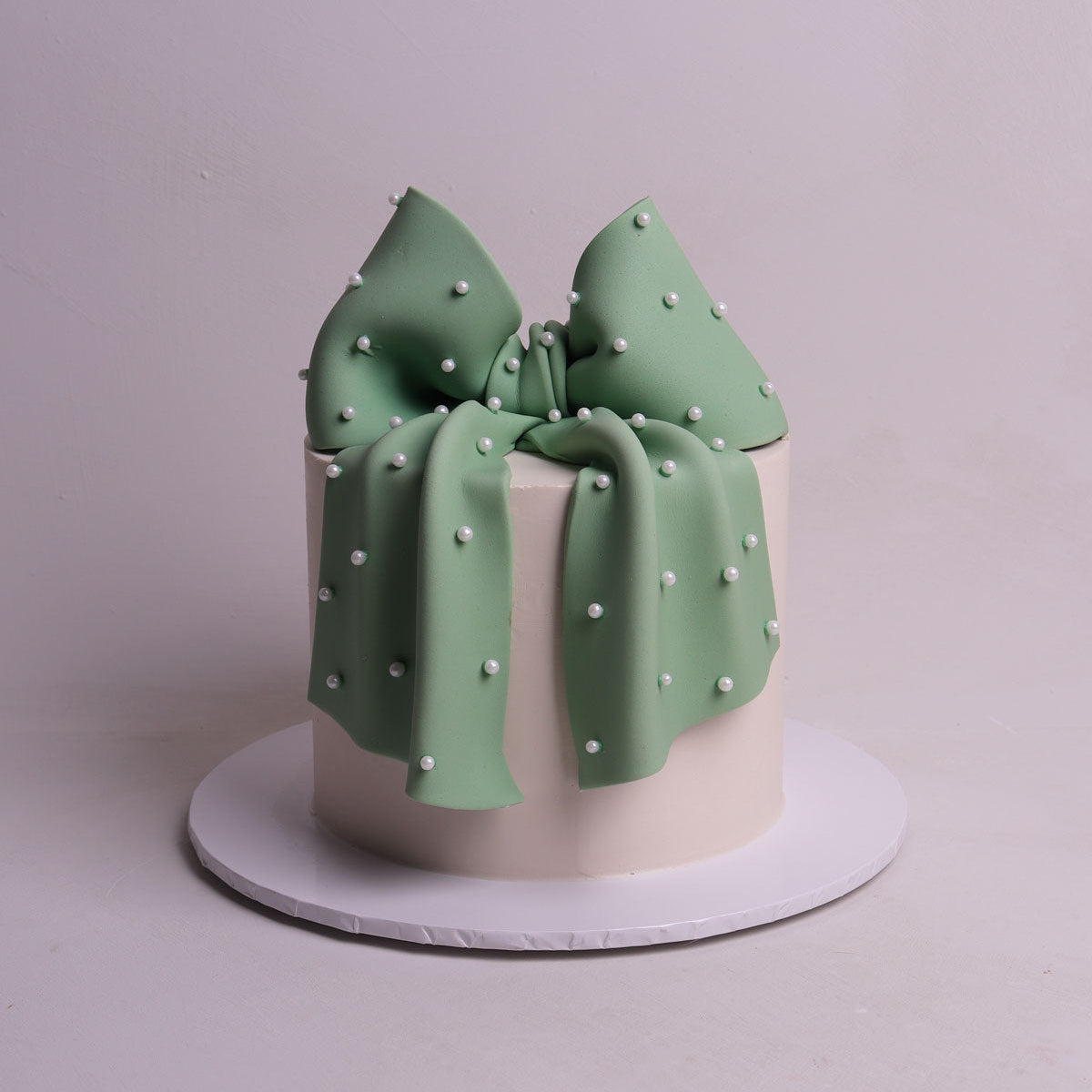 oversized sage green fondant bow with pearl detailing sitting on buttercream cake for birthday and baby shower events in Mellbourne.
