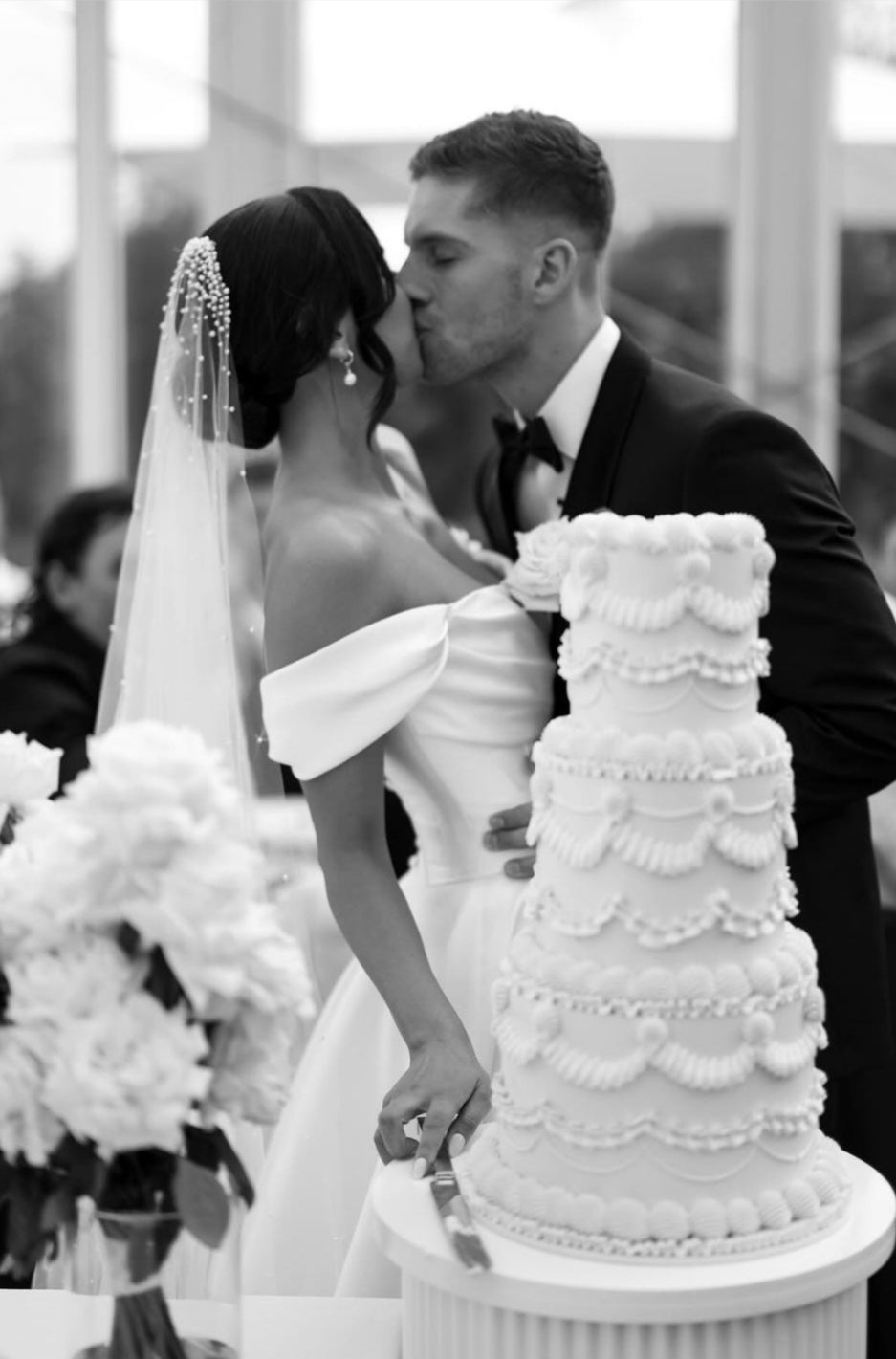 Bride and groom share a kiss beside an elegant tiered wedding cake in Melbourne, capturing a romantic moment on their special day