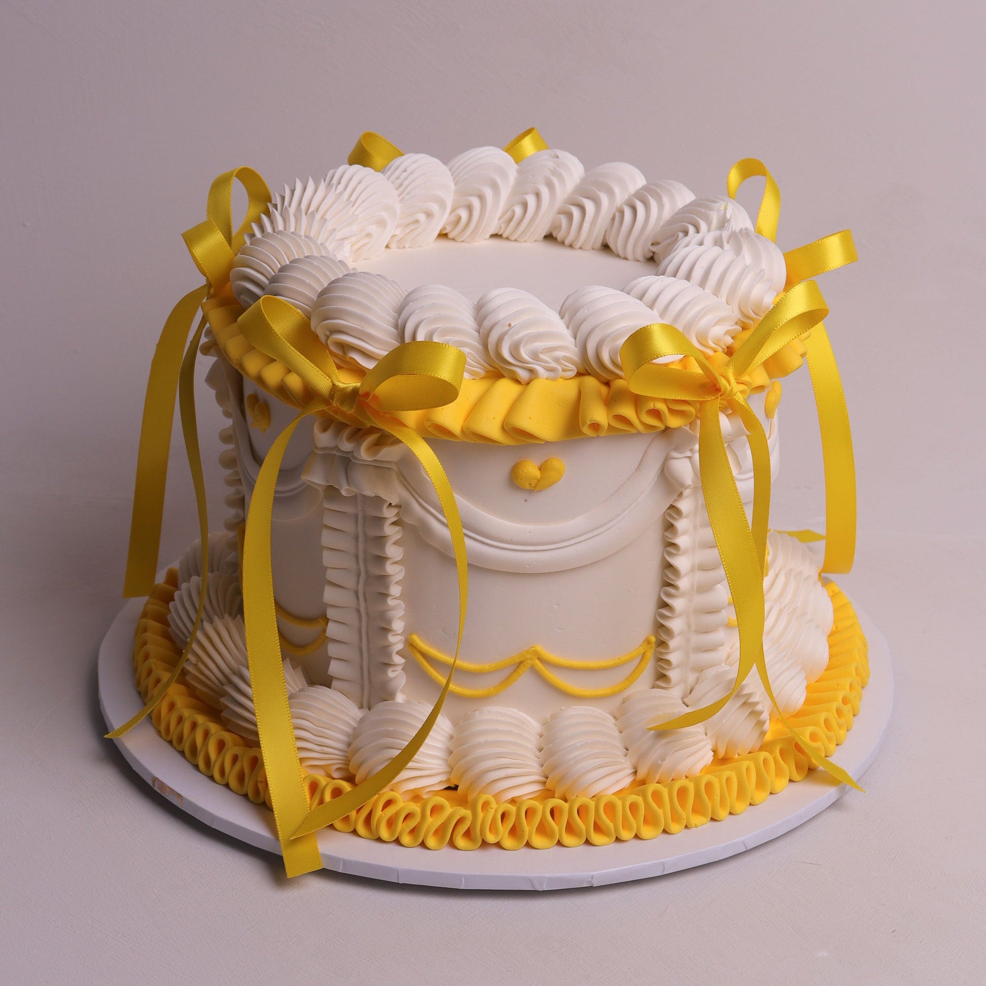 white vintage buttercream cake with yellow accent piping and yellow satin bows.