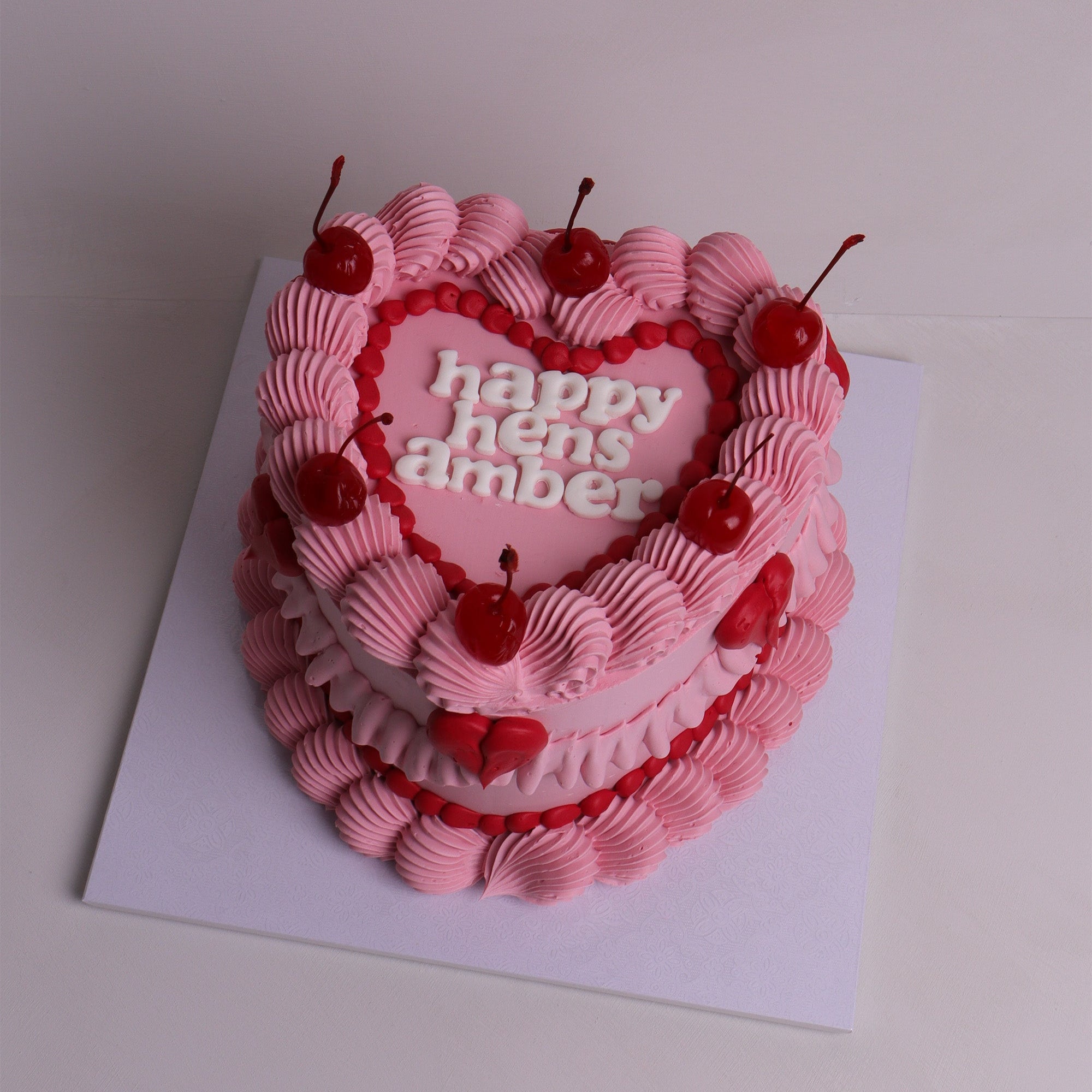 Pink heart-shaped vintage cake with piped buttercream, red cherries and retro lettering – hens party cake in Melbourne