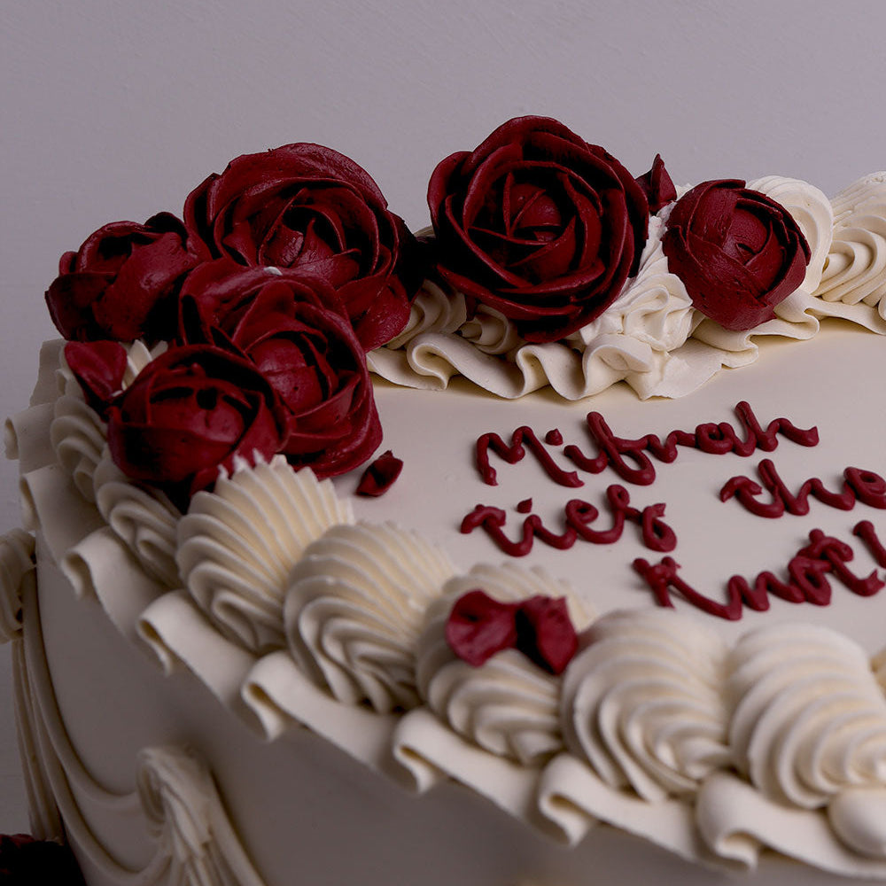 Close-up of buttercream roses in deep red with ivory piped swirls on a heart-shaped wedding cake