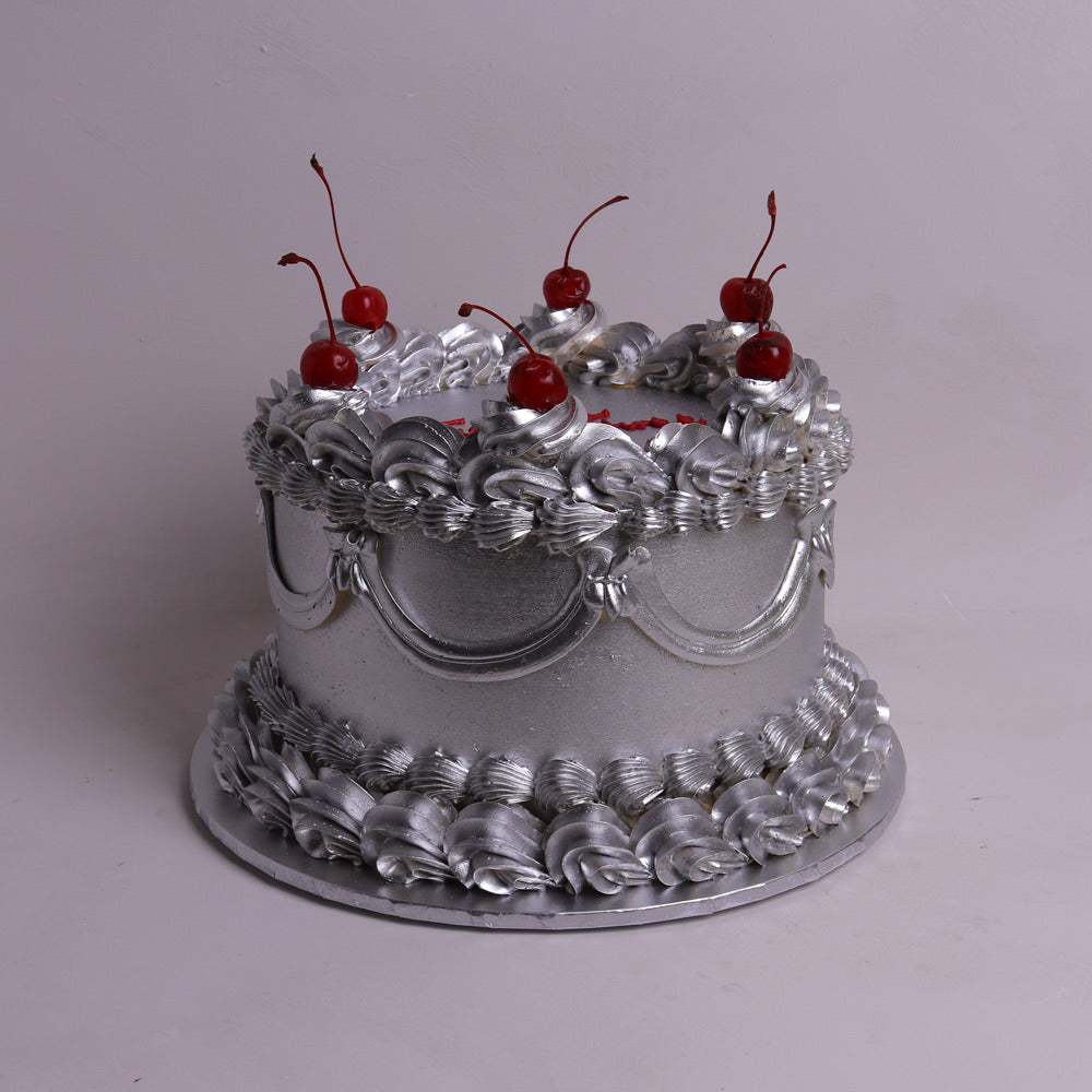 A silver cake decorated with piped frosting rosettes, draped silver ribbon, and topped with five red cherries on a silver cake board against a light gray background.