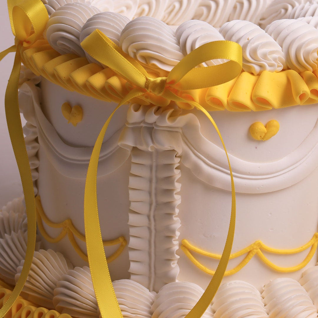Decorative cake with white frosting and yellow ribbons on a light gray background